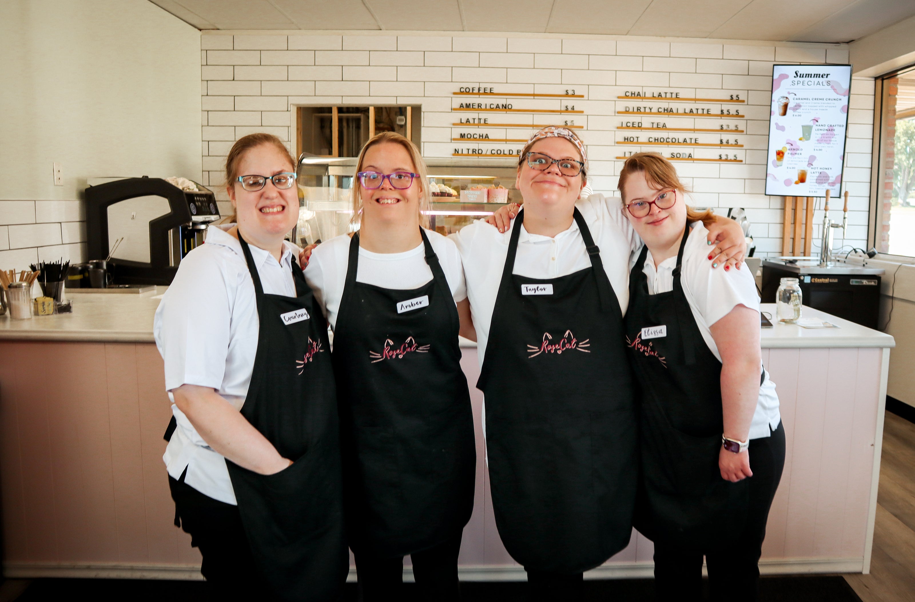 Rose Cat Baristas, Courtney, Amber, Taylor, and Elissa pose in their aprons in front of the counter.